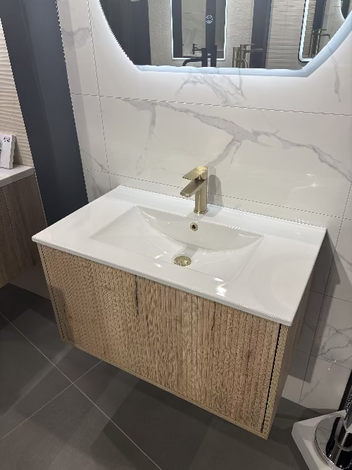Bathroom vanity with white sink and gold faucet, wooden cabinet, and marble wall.