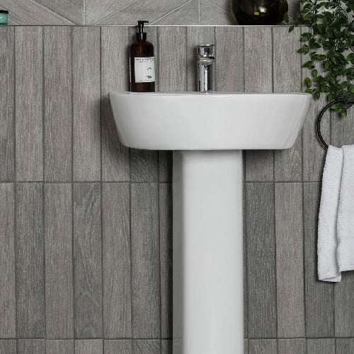 White sink with a bottle and faucet against a gray tiled wall.