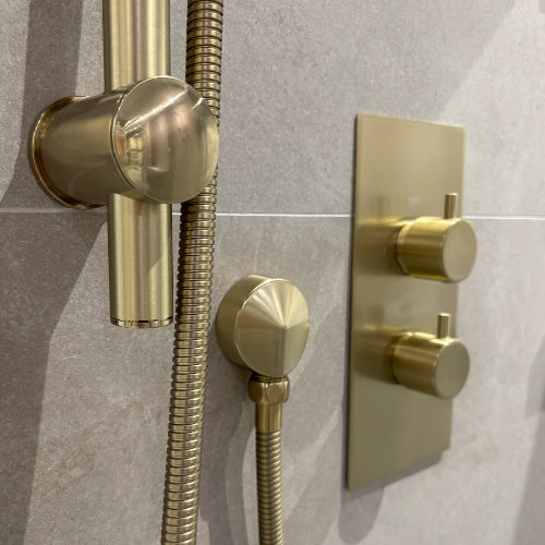 Gold shower control panel with hose on a tiled wall