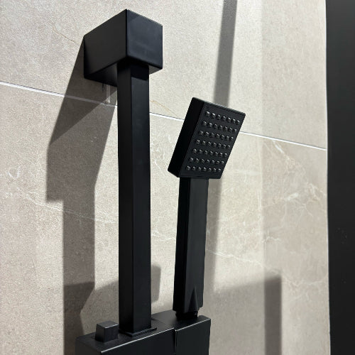 Black shower faucet and handheld shower head against a tiled wall.