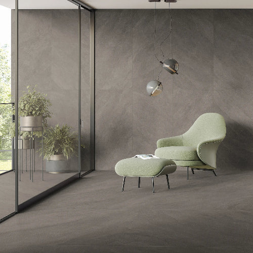 Modern green armchair and ottoman in a room with gray walls and floor.