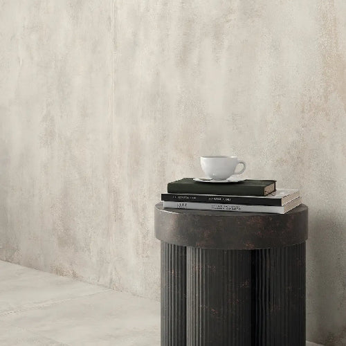 Small round dark side table with a white cup and books against a light gray wall.