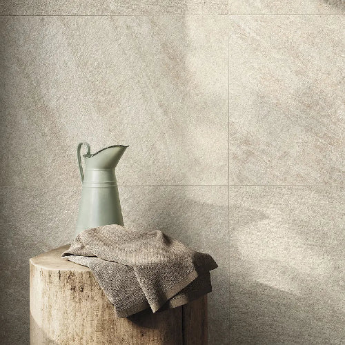 Green watering can and towel on a wooden block against a textured beige wall