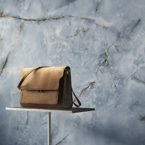 Beige leather bag on a white stand against a marble background