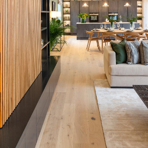 Modern living room with wooden floor, sofa, and kitchen in the background