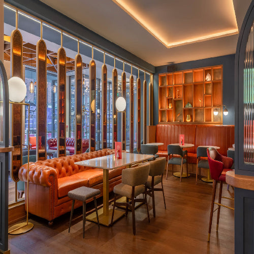 Modern restaurant interior with orange booths, wooden tables, and decorative mirrors.