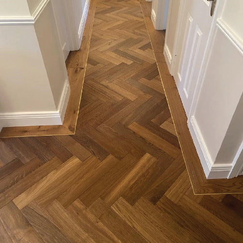 Wooden floor with herringbone pattern in a room with white walls and baseboards.