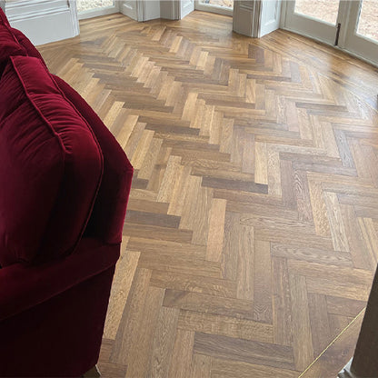 Wooden floor with herringbone pattern in a room with a red sofa.