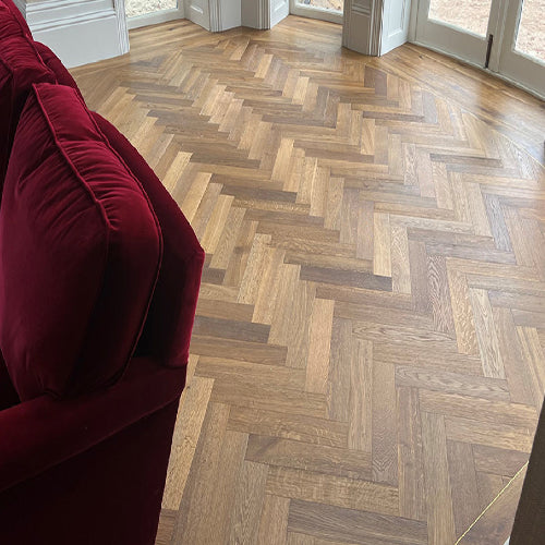 Wooden floor with herringbone pattern in a room with a red couch.