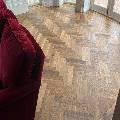 Wooden floor with herringbone pattern in a room with a red couch.