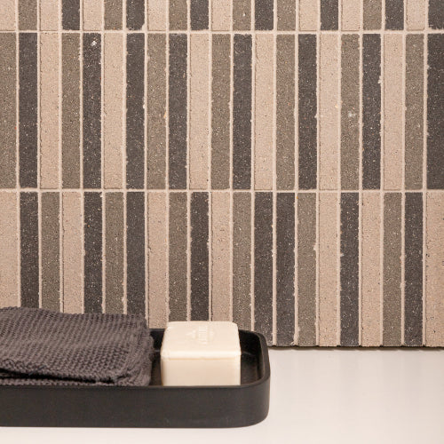 Black tray with a black towel and white bar of soap against a striped wall.