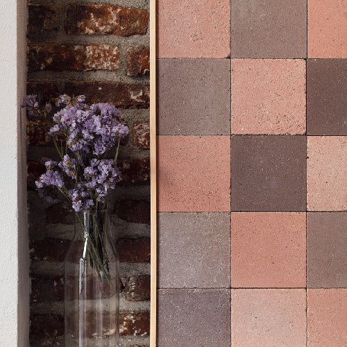 Decorative stone tiles with a vase of purple flowers on a textured wall.