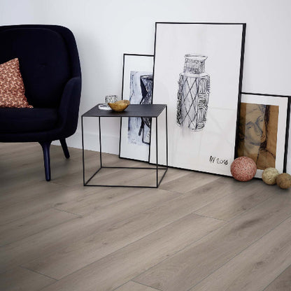 Living room with a dark armchair, small table, and framed artwork on a light wooden floor.