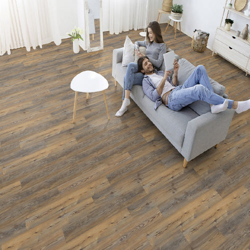 Two people sitting on a gray sofa in a room with wooden flooring.