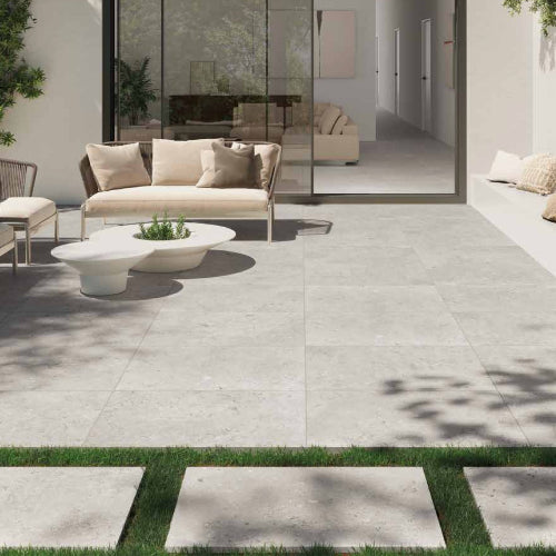 Modern outdoor patio with beige furniture and a glass wall.
