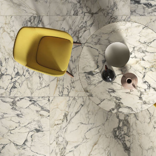Top-down view of a yellow chair and round glass table with decorative vases on a marble floor.